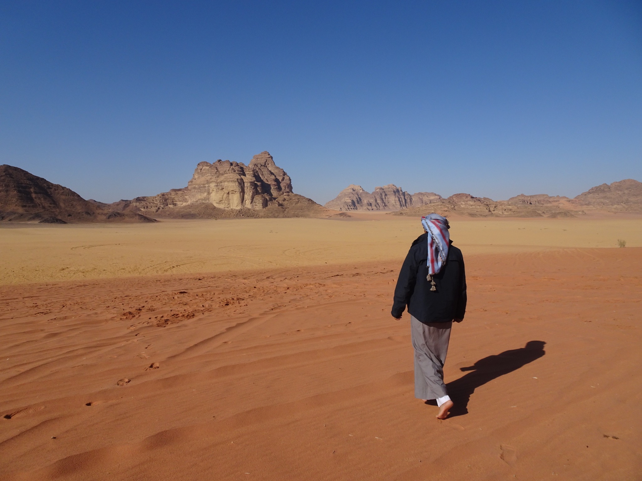 A figure walking through the open desert landscape of Wadi Rum